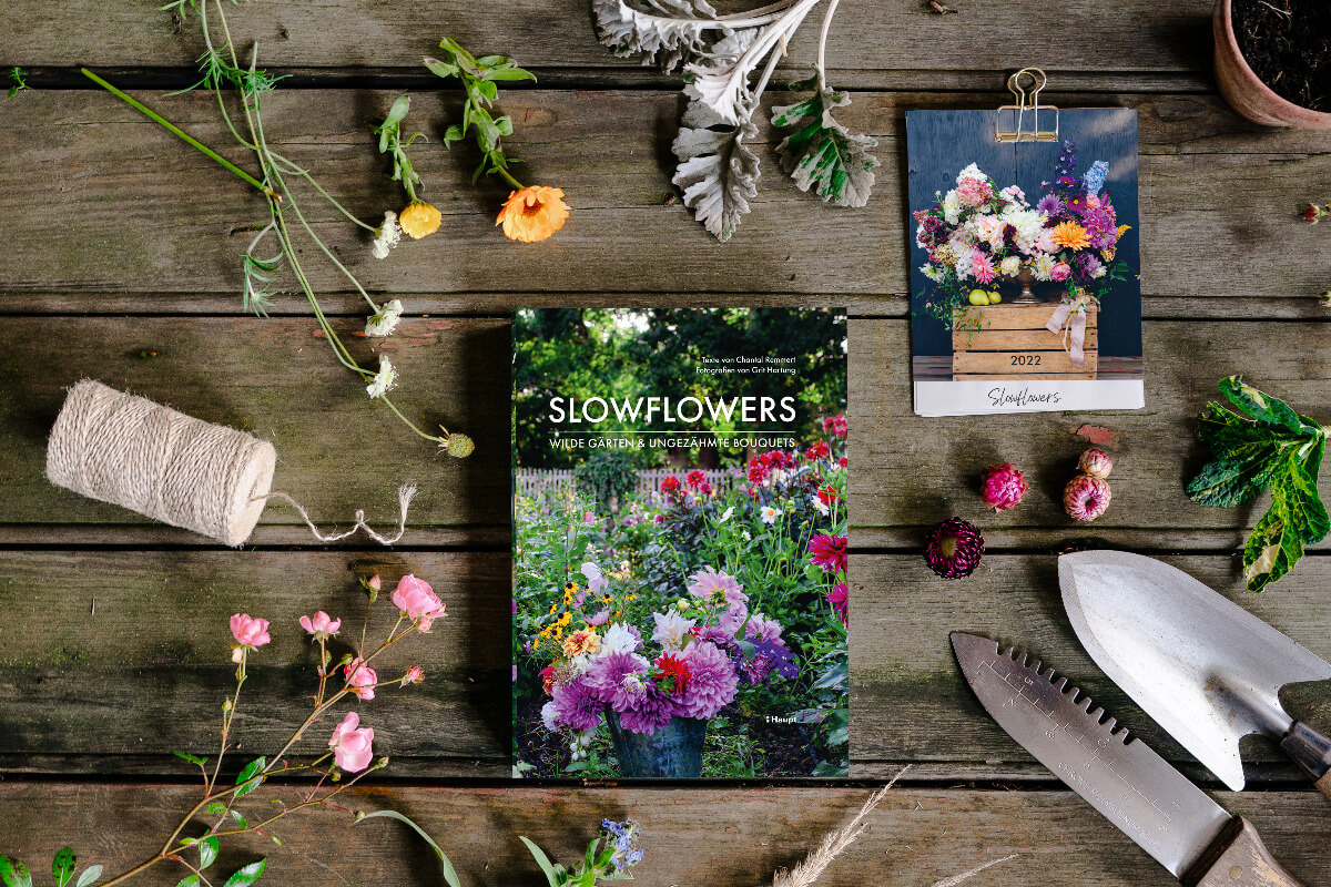 Slowflower-Buch im Zentrum, umgeben von Blüten, Gartenwerkszeug, Gartenstrick